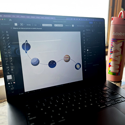Laptop screen with Illustrator on it and a series of planets appearing as objects on a simple path.