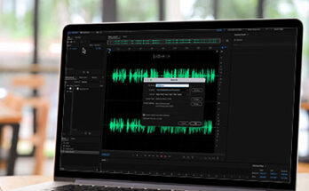 Laptop computer on wooden table with Audition waveform on screen.